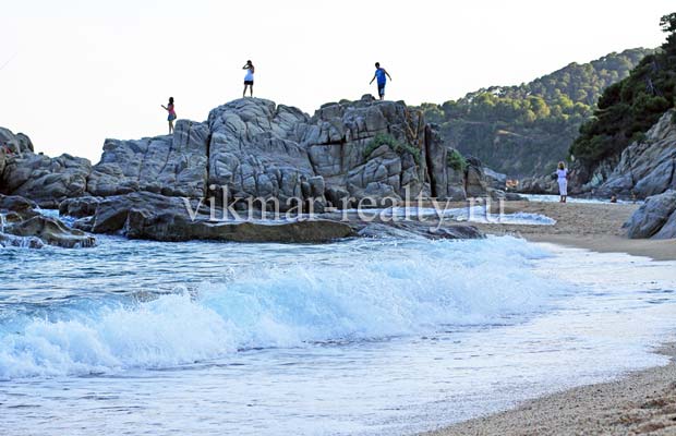 Пляж Playa de Sa Boadella в Ллорет де Мар Cкальный массив на пляже Playa de Sa Boadella на фоне мыса Punta de s'Aguia в Ллорет де Мар